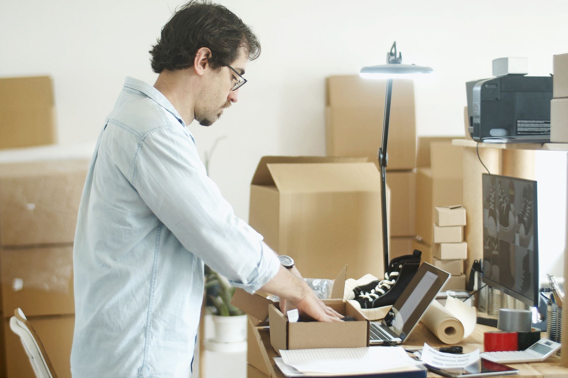 Man die vanuit een thuiskantoor producten inpakt voor een online winkel, als voorbeeld van extra inkomen vanuit huis.
